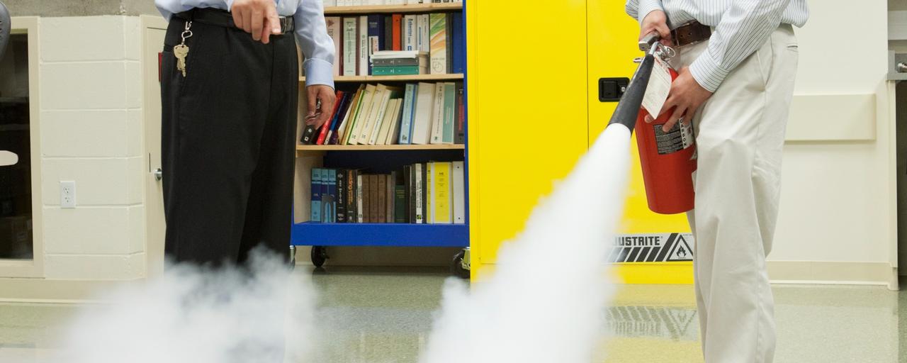 Fire extinguisher blowing out a fire with a professor and student standing nearby